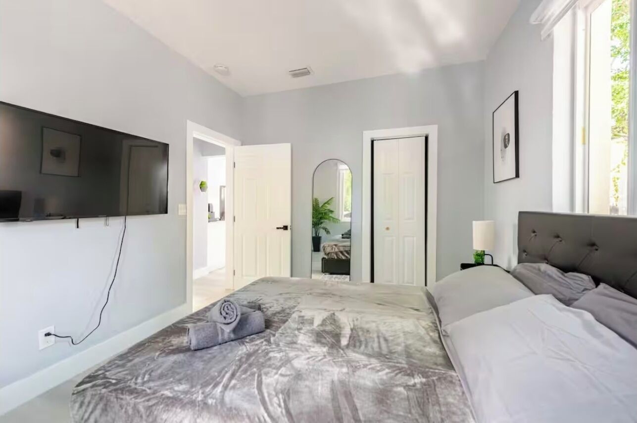 Quarto com cama, televisão fixada na parede, porta e janela.