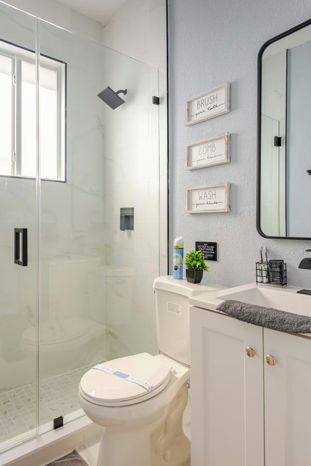 A modern bathroom with a glass shower enclosure, a toilet, a sink with a mirror, and wall-mounted storage.