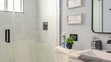 A modern bathroom with a glass shower enclosure, a toilet, a sink with a mirror, and wall-mounted storage.