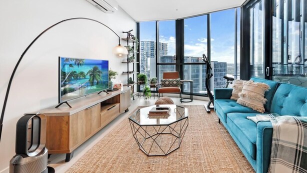 Ein modernes Wohnzimmer mit großem Fernseher, einer Couch, einem Couchtisch und Blick auf die Stadt durch große Fenster.