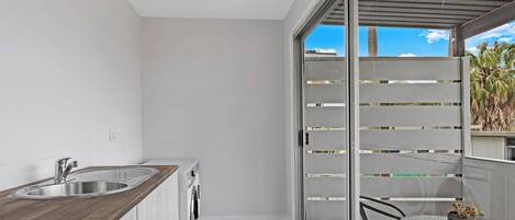 A balcony with a sliding glass door, a small table with chairs, and a kitchen area with a sink and washing machine.