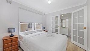 Un dormitorio con cama, mesitas de noche, cómoda, armario y baño con espejo y lavamanos.