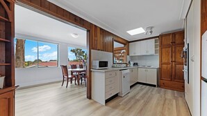 Una cocina con armarios de madera, microondas, lavavajillas y un comedor con sillas y mesa.