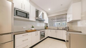A modern kitchen with white cabinetry, stainless steel appliances, and a window with decorative bars.