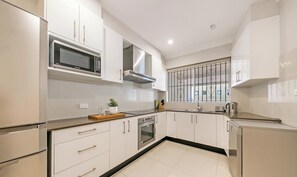 A modern kitchen with white cabinetry, stainless steel appliances, and a window with decorative bars.