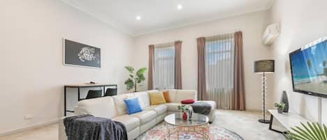 Een woonkamer met een bank, salontafel, televisie en gordijnen.