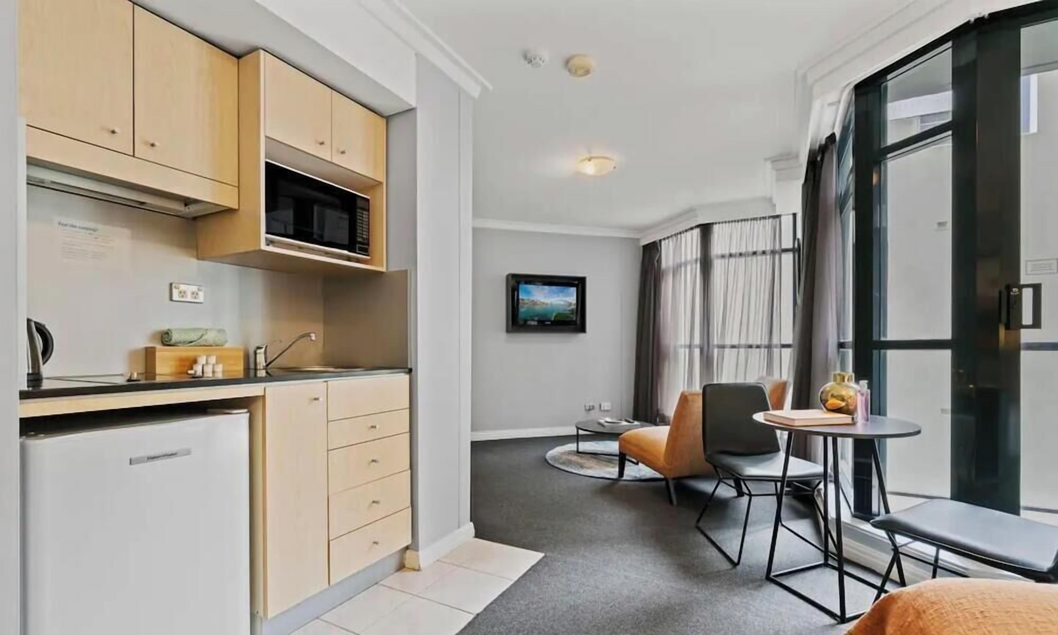 A compact kitchen with modern appliances, a dining area with a small table and chairs, and a large window with curtains.