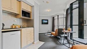 A compact kitchen with modern appliances, a dining area with a small table and chairs, and a large window with curtains.