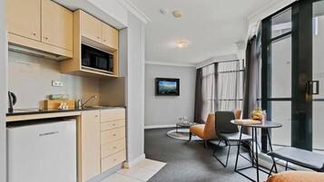 A compact kitchen with modern appliances, a dining area with a small table and chairs, and a large window with curtains.