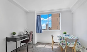 A small room with a desk, chair, table, and window.
