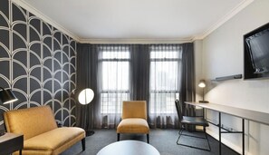 Una habitación de hotel con sofá, sillón, escritorio y televisor.