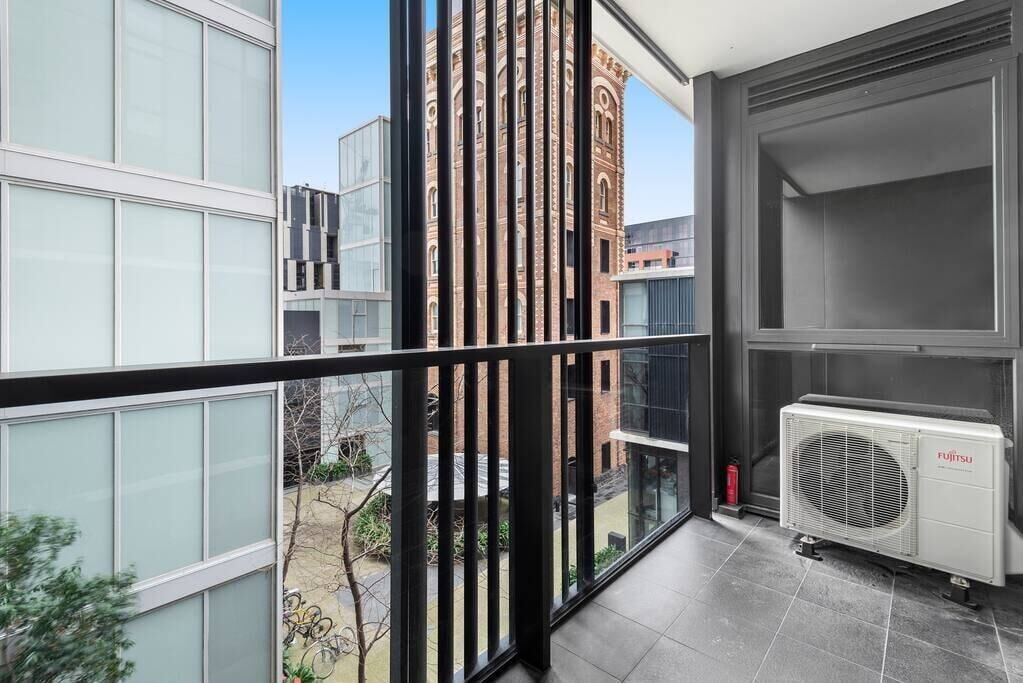 A modern apartment with large windows, a view of a brick building, and a Fujitsu air conditioning unit.