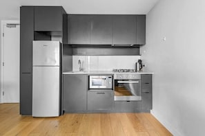 A modern kitchen with grey cabinets, a built-in microwave, oven, and a refrigerator. - KozyGuru | Collingwood | Stylish 1 Bed Apt (Collingwood)