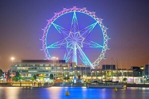A large Ferris wheel with a star-like structure, surrounded by buildings and a waterfront. - KozyGuru | Collingwood | Stylish 1 Bed Apt (Collingwood)