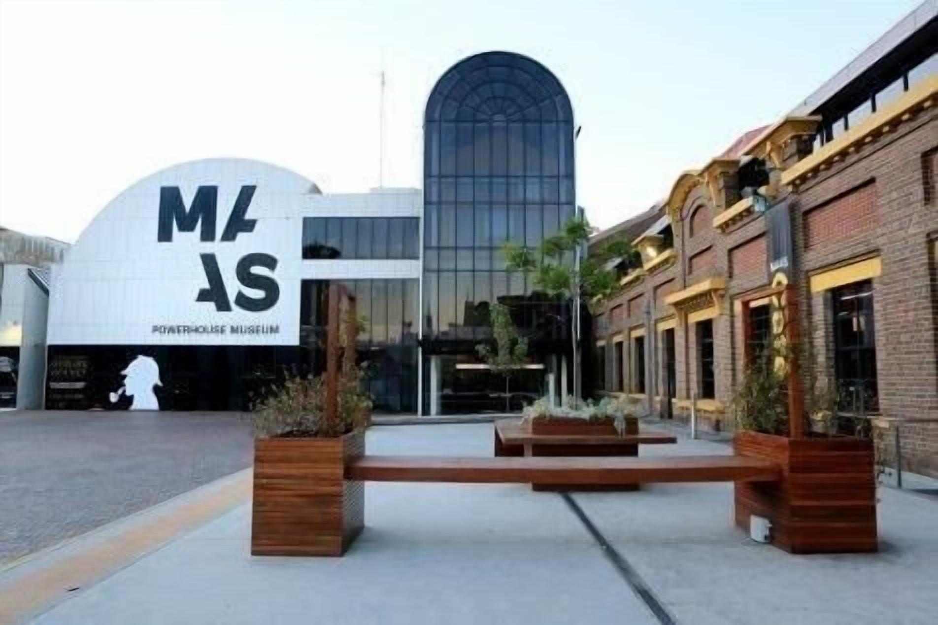 A modern building with a large 'M' and 'S' sign, likely a museum, with a glass facade and a traditional brick building nearby.