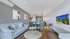 En moderne stue med en grå sofa, et sofabord og et spiseområde med et køkken i baggrunden.