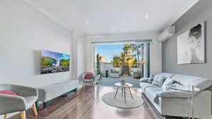 En moderne stue med en sofa, lænestol og sofabord. Et maleri hænger på væggen, og der er udsigt til en udendørs patio.