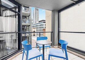 Un balcon avec une table et des chaises, une vue sur les immeubles et une fenêtre avec des rideaux.