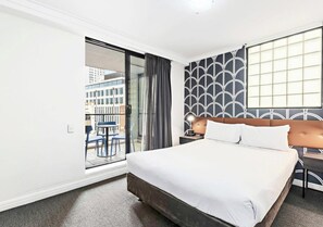 Une chambre d’hôtel avec un lit, une fenêtre avec des rideaux, un mur à motifs et une vue sur les bâtiments environnants.