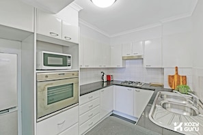 A modern kitchen with white cabinets, a microwave, an oven, a gas stove, and a sink.