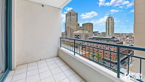 A balcony with a city view, a tiled floor, and a metal railing.