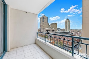 A balcony with a city view, tiled floor, and a metal railing. - KozyGuru | Haymarket Syd | Overly Warm | 1 Bed Apt (Haymarket)