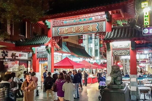 A bustling night market with traditional architecture and red lanterns.