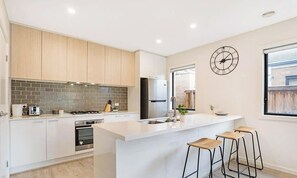 A modern kitchen with a central island, stainless steel appliances, and wooden bar stools.