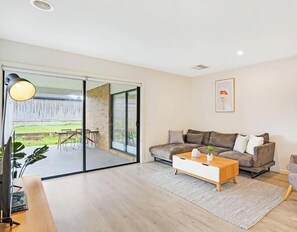 A modern living room with a sofa, coffee table, and a sliding glass door leading to an outdoor area.
