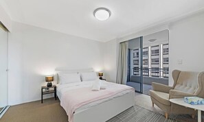 Ein Hotelzimmer mit Bett, Nachttischlampen, einem Sessel, einem Tisch und einem Balkon mit Blick.