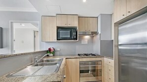 A modern kitchen with a stainless steel refrigerator, a built-in microwave, a gas stove, and wooden cabinets. - CBD - 2BR in Heart of Sydney, light rail at door (Haymarket)