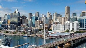A city skyline with modern skyscrapers, a waterfront promenade, and a bridge. - CBD - 2BR in Heart of Sydney, light rail at door (Haymarket)