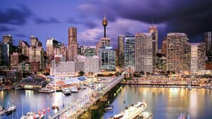 A city skyline with a prominent tower, a marina with boats, and a bridge connecting two areas. - CBD - 2BR in Heart of Sydney, light rail at door (Haymarket)