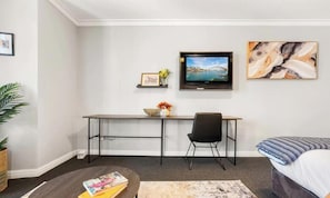 A hotel room with a bed, a desk with a chair, a television, and artwork on the wall.