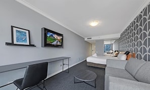 Ein modernes Hotelzimmer mit einem Bett, einem Schreibtisch, einem Stuhl, einem Fernseher und einem Sofa.