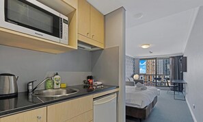 Eine moderne Küche mit Mikrowelle, Spüle und Wasserkocher, ein kleiner Essbereich und ein Schlafzimmer mit Bett und Blick auf die Stadt.
