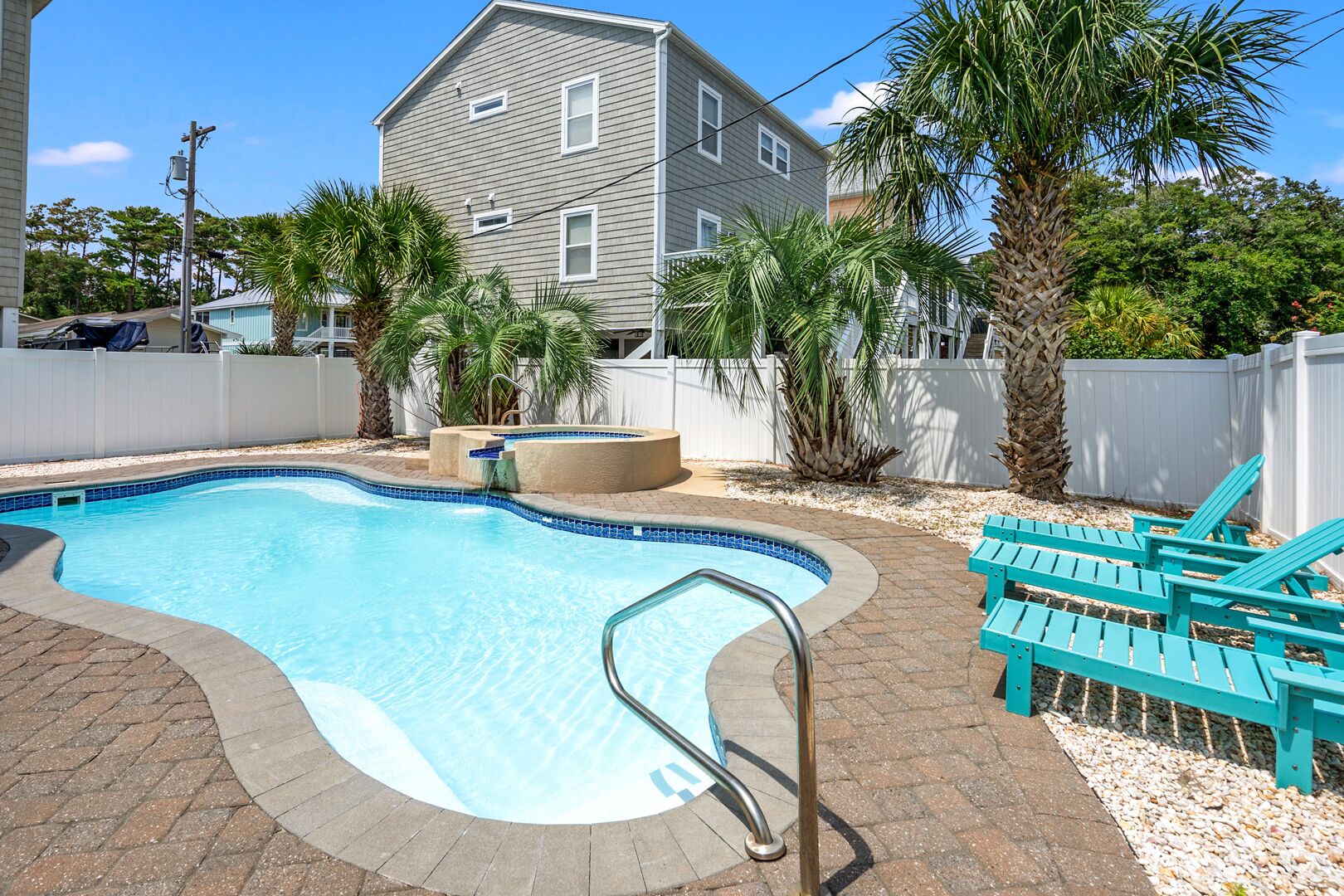 A swimming pool with a tiled edge, a metal ladder, and a lounge area with chairs.