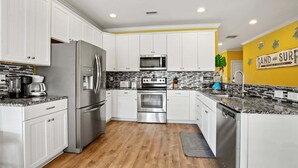 A modern kitchen with white cabinets, stainless steel appliances, a wooden floor, and a yellow accent wall. - Luxury home w/private pool, walking distance to the beach, eateries and shopping (North Myrtle Beach)