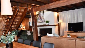 A cozy living room with a wooden staircase, a fireplace, a television, and a dining area with a wooden table and chairs. - Diskin House Mt Pleasant Rd, Eltham. Great for weddings - 2 Kms to Montsalvat. (Eltham)