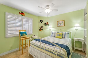 A bedroom with a bed, a chair, a desk, a ceiling fan, and wall decorations. - Oceanfront 2BR/2BA Condo in Oceanside with Amazing Beach Access has AC! (Oceanside)