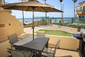 An outdoor patio with a table and chairs, a grill, and a view of the beach. - Oceanfront 2BR/2BA Condo in Oceanside with Amazing Beach Access has AC! (Oceanside)