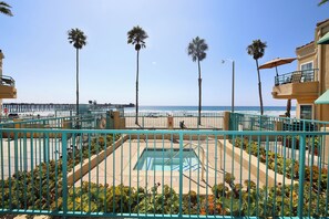 A pool area with a view of the beach and ocean, surrounded by palm trees and a fence. - Oceanfront 2BR/2BA Condo in Oceanside with Amazing Beach Access has AC! (Oceanside)