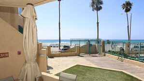 A balcony with a view of the beach, a covered patio area, and a small lawn. - Oceanfront 2BR/2BA Condo in Oceanside with Amazing Beach Access has AC! (Oceanside)