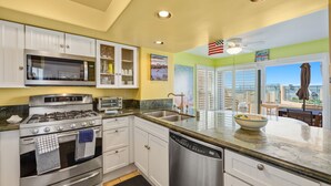A kitchen with white cabinets, stainless steel appliances, a dishwasher, and a large window with a view. - Oceanfront 2BR/2BA Condo in Oceanside with Amazing Beach Access has AC! (Oceanside)
