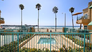 A pool area with a blue fence, palm trees, and a view of the ocean. - Oceanfront 2BR/2BA Condo in Oceanside with Amazing Beach Access has AC! (Oceanside)