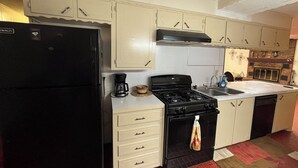 Una cocina con refrigerador negro, estufa y armarios blancos.