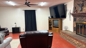 Una sala de estar con alfombra roja, sofás de cuero, un televisor de pantalla plana, chimenea y un ventilador de techo.