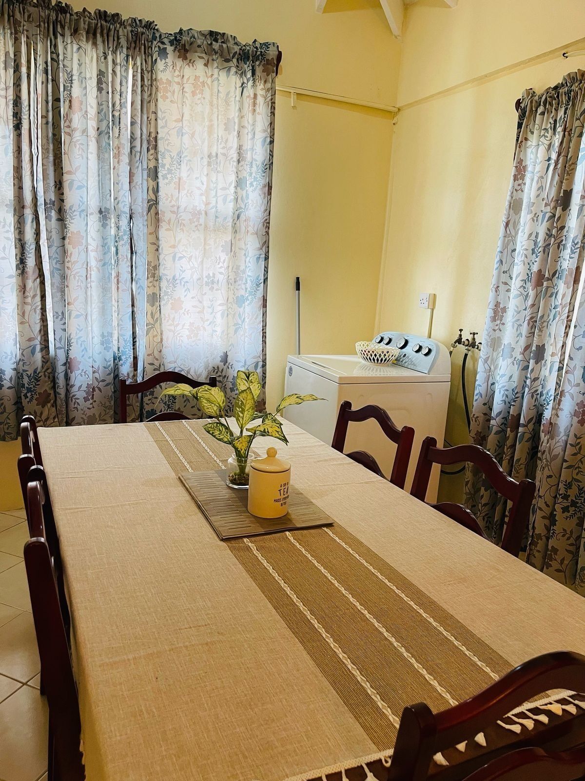 A dining area with a table set for four, a washing machine, and floral curtains.