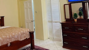 A bedroom with a bed, dresser, television, and a door. - Castle Berry Apartments  (Brighton)