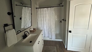 A bathroom with a sink, mirror, and shower curtain. - Charming cottage with WiFi and AC on a Ranch setting in Oakdale (Oakdale)